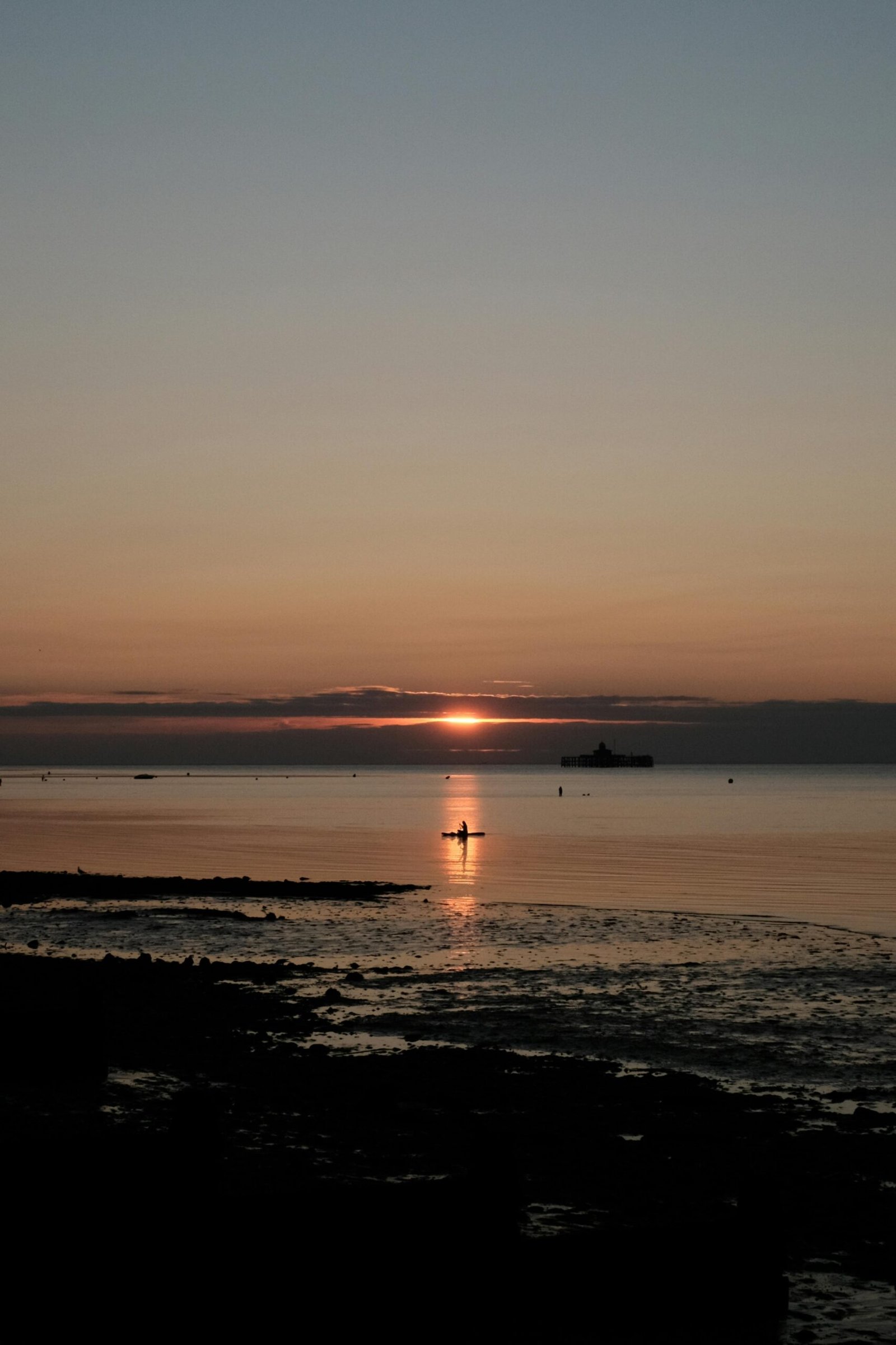 Serene sunset view with silhouetted boat on calm ocean at dusk.